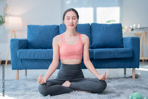 Relaxed asian woman practicing yoga, meditating in lotus pose at home, enjoying healthy lifestyle, promoting mindfulness and stress relief through physical and mental wellness