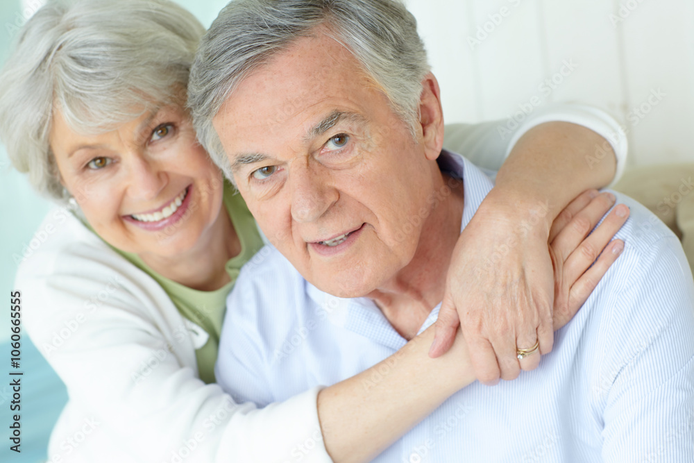 Hug, portrait and smile of senior couple on sofa in living room of home together for bonding or commitment. Face, love or retirement with old man and woman embracing in apartment for safety or trust Hug, portrait and smile of senior couple on sofa in living room of home together for bonding or commitment. Face, love or retirement with old man and woman embracing in apartment for safety or trust