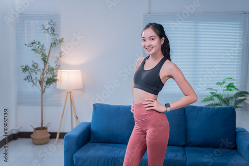 Young asian woman wearing sportswear is posing in her living room after finishing her home workout, demonstrating confidence and a healthy lifestyle