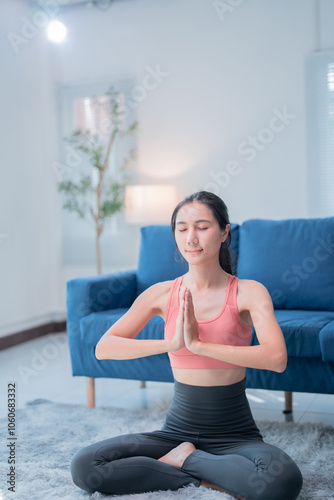 Relaxed asian woman practicing yoga, meditating in lotus pose at home, enjoying peaceful atmosphere, promoting mental health and well-being through mindfulness