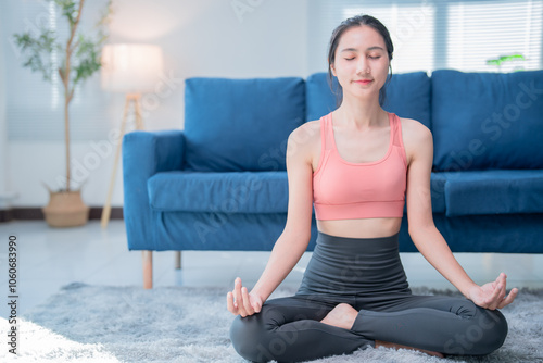 Asian woman doing yoga at home, finding peace and balance in lotus pose, promoting healthy lifestyle and mindfulness