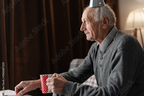 Lonely forgotten by children old man celebrating birthday alone drinking tea at home. Copy space. photo