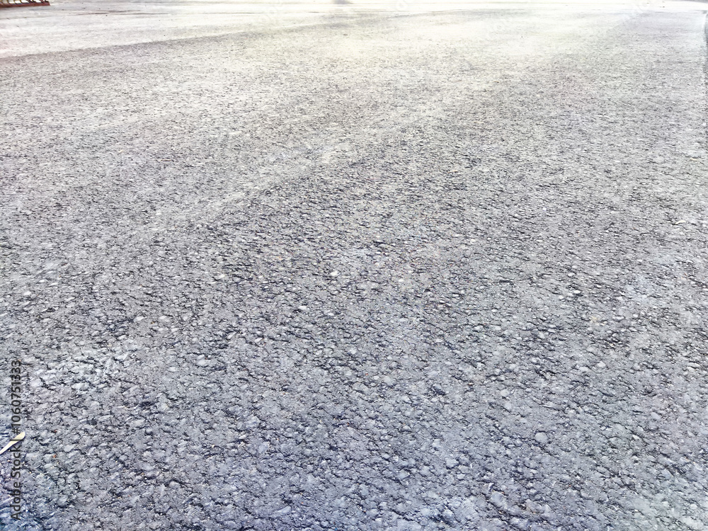 A close up view of an asphalt road surface, showing its rough texture and the sun reflecting off its surface. Background, texture, pattern, frame A close up view of an asphalt road surface, showing its rough texture and the sun reflecting off its surface. Background, texture, pattern, frame