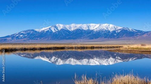 A snow-capped mountain range reflected in a calm lake with a blue sky.