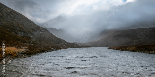 The wind whips across the water, creating a swirling, textured surface, as the fog rolls in and enshrouds the surrounding hills in a veil of mystery and quiet awe. photo