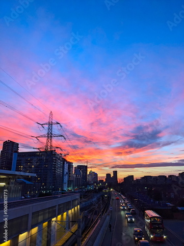 London, UK - 02.01.2024: Pink and golden evening glow over Custom House Elizabeth Line station alongside cars and a bus queuing before a red light 