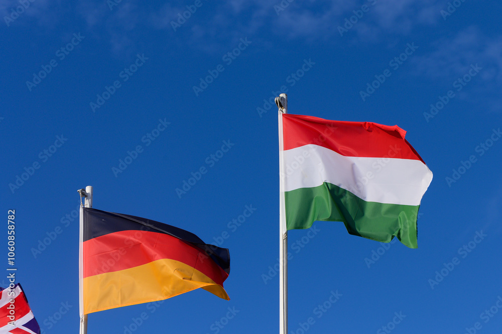 Colorful flags of Germany and Hungary waving under a bright blue sky on a sunny afternoon Colorful flags of Germany and Hungary waving under a bright blue sky on a sunny afternoon