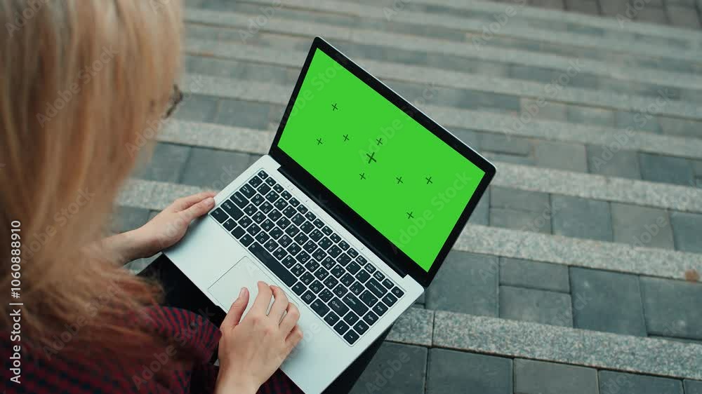Woman working on laptop with green screen outdoors