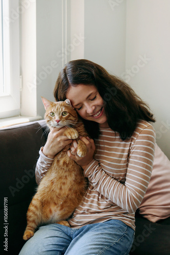 Brunette young woman playing with her rescue red cat at home. Copy space background.