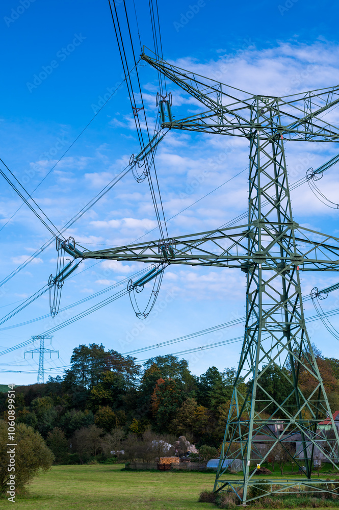 A landscape photo of power lines and transmission towers stretching across an open field with a scenic backdrop of hills and a partly cloudy sky.
