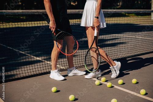 Shot of slender legs of a sporty tennis couple. Slender sporty legs in sneakers on a tennis court