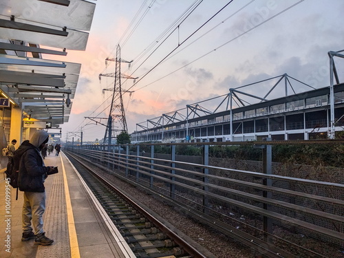 London - 03.08.2024: Passengers waiting for a train at the Custom House Elizabeth Line station behind the yellow line next to the Excel Exhibition Centre during dawn with a pink sky