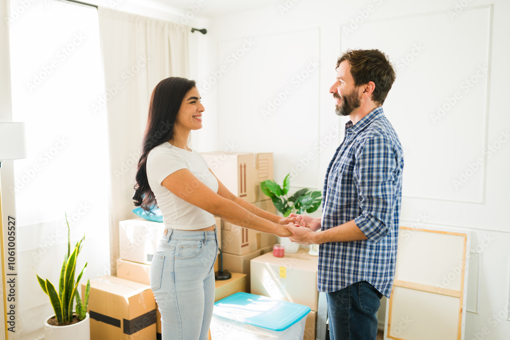 Newly moved-in young couple holding hands and gazing at each other in their living room, celebrating their new home Newly moved-in young couple holding hands and gazing at each other in their living room, celebrating their new home