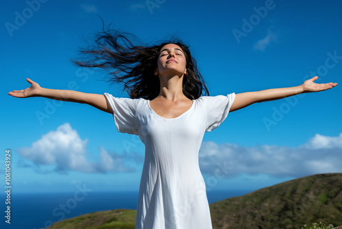 A woman stands atop a hill with her arms wide open, eyes closed, and face lifted toward the sky, embracing the fresh air and tranquility of the open landscape, symbolizing freedom and inner peace.