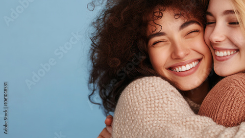 Two female friends embracing joyfully against a light blue background, capturing a moment of happiness and friendship, emale friendship and support photo