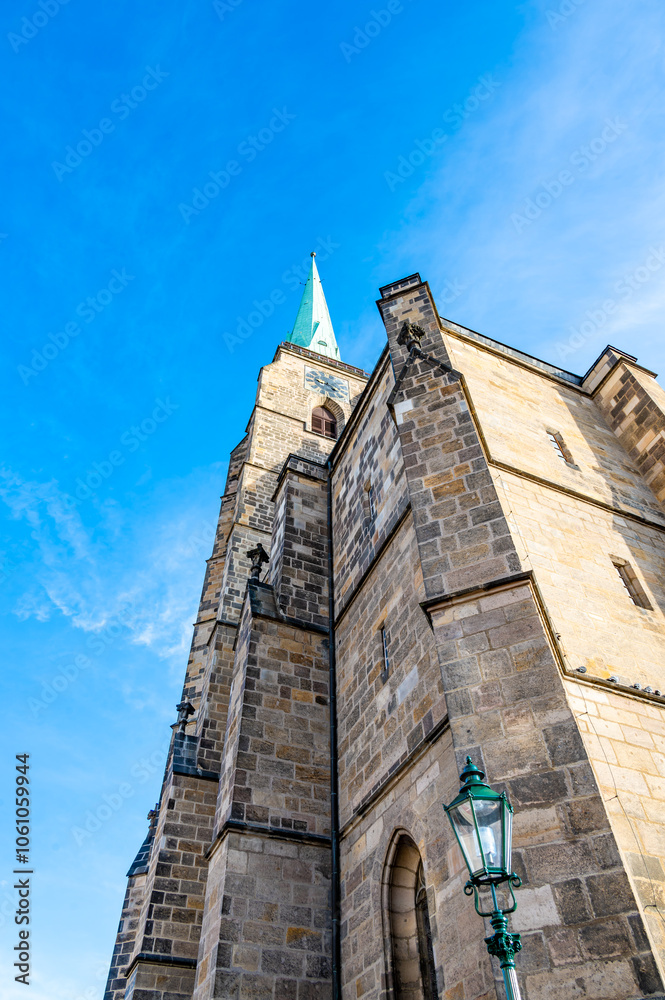 A photograph of the Cathedral of St. Bartholomew in Plzen, Czech Republic. This Gothic cathedral with its iconic tower stands proudly, surrounded by historic buildings, offering a stunning view
