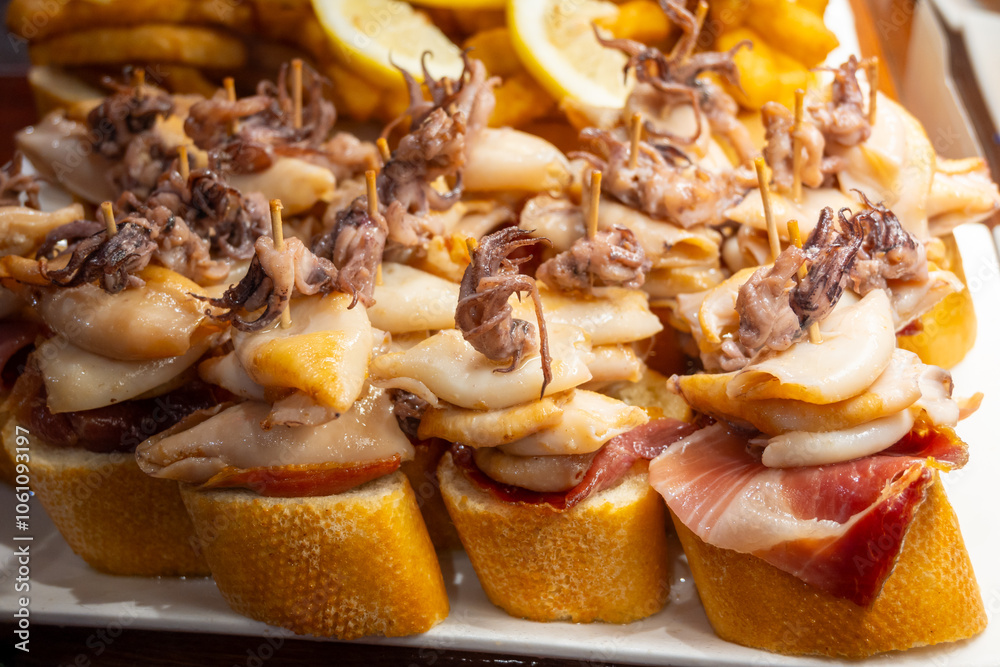 Fototapeta premium Typical snacks of Basque Country, pinchos or pinxtos skewers with small pieces of bread, fish, sea food, sweet green pepper served in bar in San-Sebastian or Bilbao, Spain