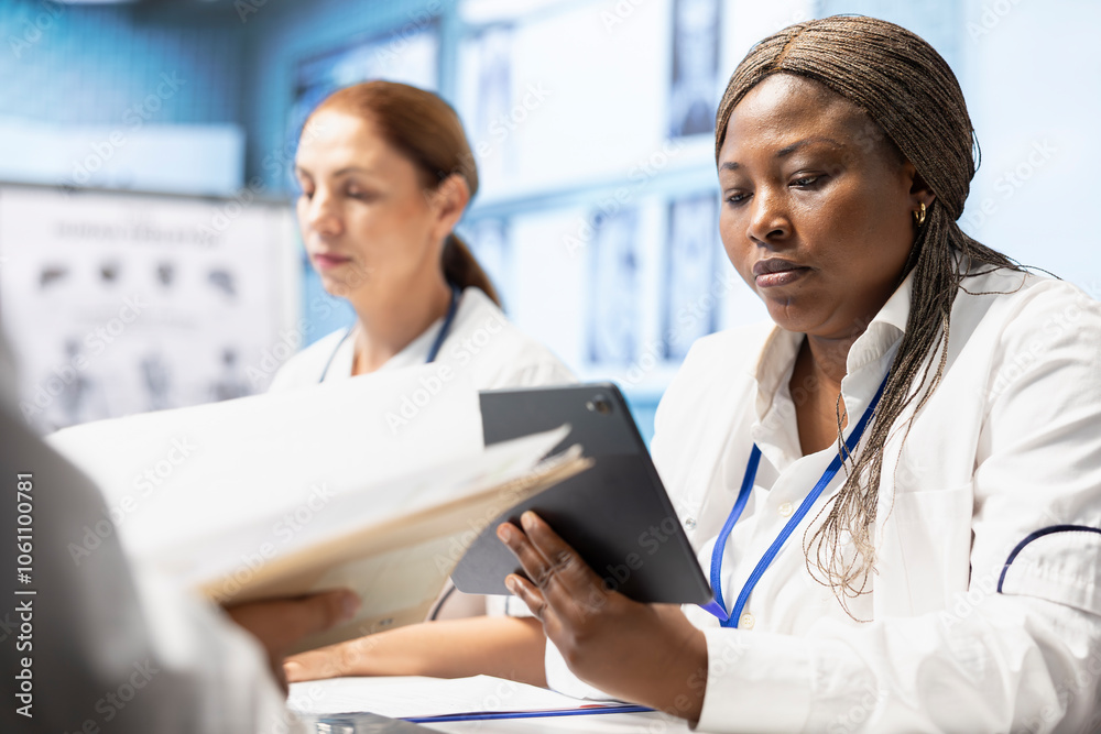 Diverse team of doctors discuss x ray results in a treatment center meeting, looking at radiography scans to ensure the right treatment. Licensed medics developing disease prevention strategies. Diverse team of doctors discuss x ray results in a treatment center meeting, looking at radiography scans to ensure the right treatment. Licensed medics developing disease prevention strategies.