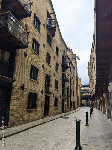 London, UK - 05.13.2024: A quiet time of Shad Thames with converted warehouses and elevated walkways over the tiled floor and shops on the ground floor under a cloudy sky without tourists photo