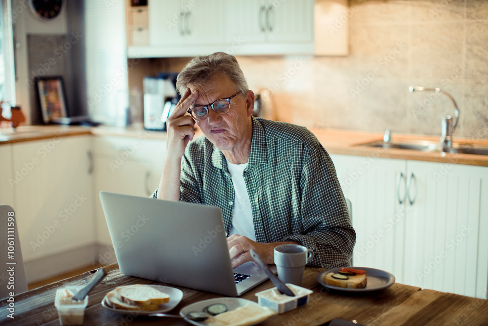 Senior mature man using laptop on kitchen table Senior mature man using laptop on kitchen table