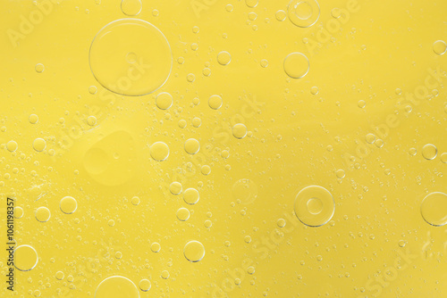 Essential oil bubbles on yellow background, macro view. Cosmetic product