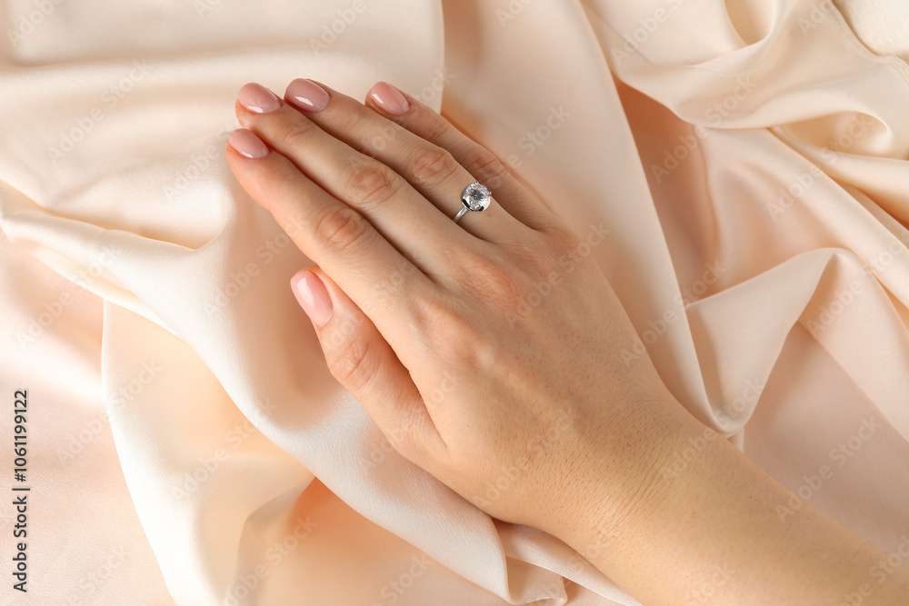 Woman wearing beautiful ring with gemstone against beige fabric, closeup Woman wearing beautiful ring with gemstone against beige fabric, closeup