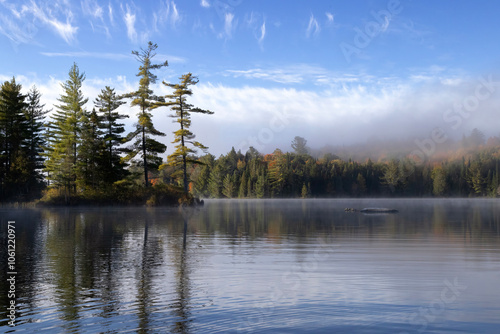 Reflection of trees in a peaceful early morning on misty Joe Lake in Algonquin Provincial Park Ontario Canada