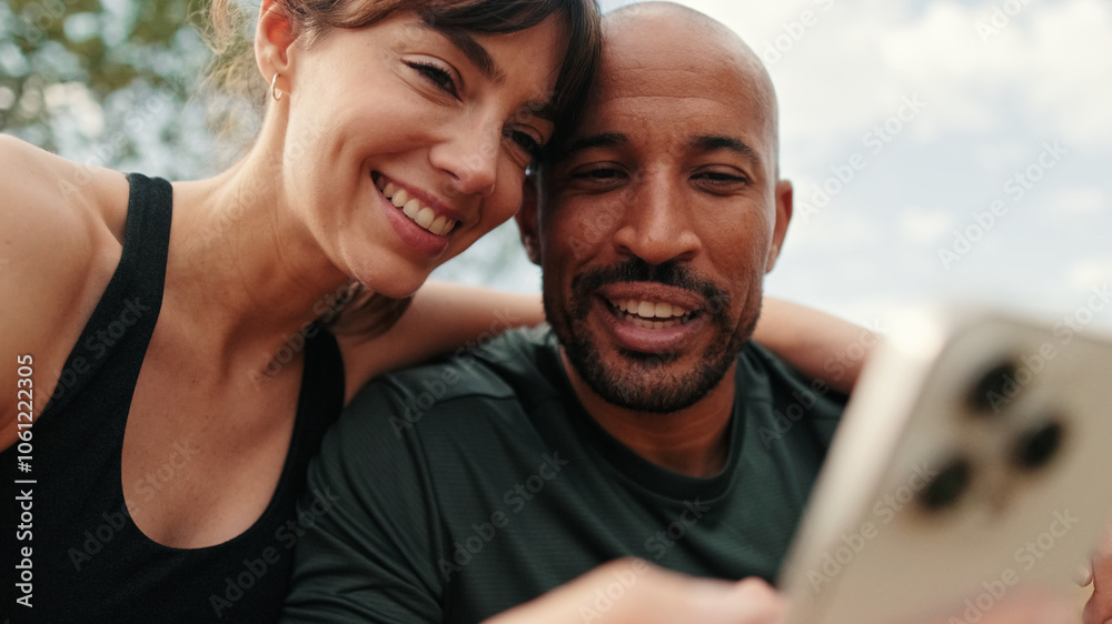 Close-up of athletic couple in love relaxing and using smartphone, focus on persons Close-up of athletic couple in love relaxing and using smartphone, focus on persons