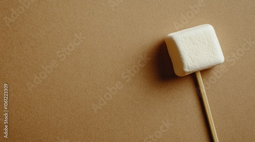 A Single Marshmallow on a Wooden Stick Against a Brown Background photo