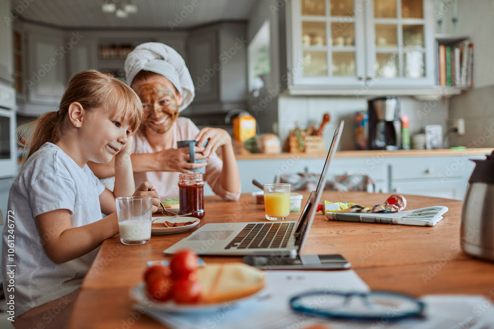 Mother and daughter having breakfast and watching laptop together in cozy kitchen Mother and daughter having breakfast and watching laptop together in cozy kitchen