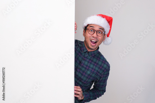 A man wearing christmas hat peeking from behind a wall showing amazed expression photo