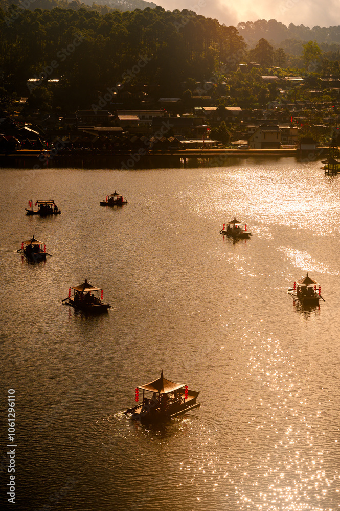 Φωτογραφία A traditional wooden boat adorned with red lanterns floats peacefully on the serene waters of Ban Rak Thai Village, surrounded by misty mountains at sunrise