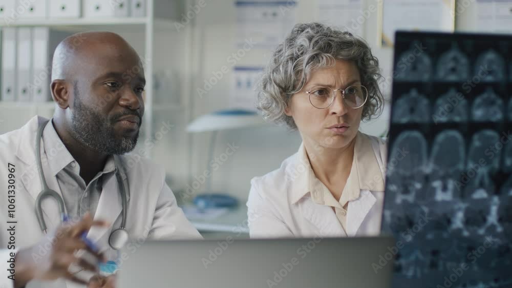 Two professional doctors closely examining brain MRI scan, evaluating symptoms and discussing diagnosis during workday in medical office