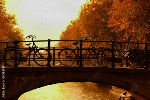 Photography Autumn cityscape, Silhouette of classic bicycles parked on Amsterdam canal bridg
