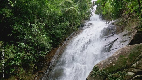 Rapid fresh water falling from the top of the mountain through the rocky cliff surrounded by green plants in tropical rainforest. Stunning waterfall in Phang Nga Province, Thailand.