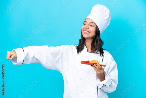 Young hispanic chef woman holding sashimi isolated on blue background giving a thumbs up gesture photo