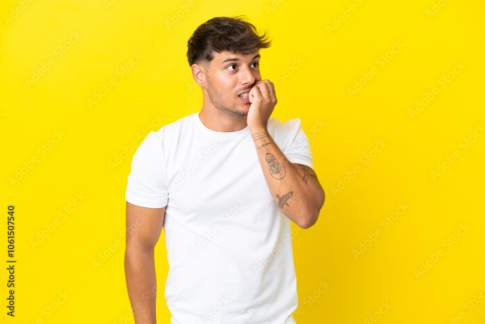 Young caucasian handsome man isolated on yellow background is a little bit nervous Young caucasian handsome man isolated on yellow background is a little bit nervous