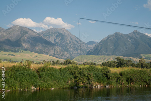 A fly fishing rod in the foreground over a creek with mountains photo