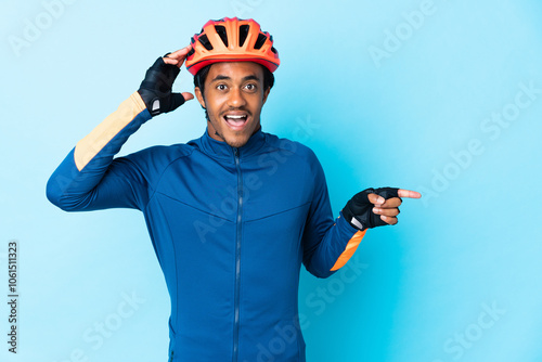 Young cyclist man with braids over isolated background surprised and pointing finger to the side photo