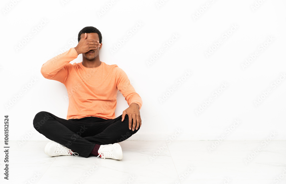 African American man sitting on the floor over isolated copyspace background covering eyes by hands. Do not want to see something African American man sitting on the floor over isolated copyspace background covering eyes by hands. Do not want to see something