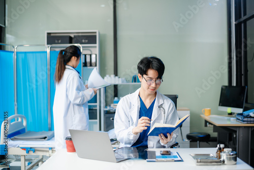 Confident young doctor in white medical uniform sit at desk working on computer. Smiling use laptop write