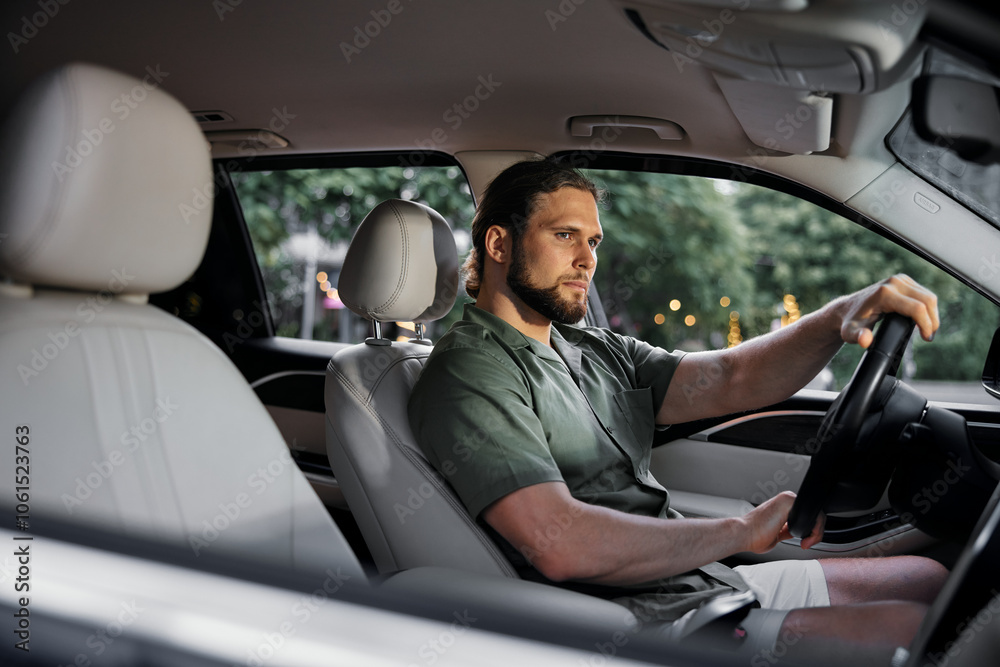 Man driving a car with a serious expression, focused on the road, interior view with blurred greenery in the background Man driving a car with a serious expression, focused on the road, interior view with blurred greenery in the background