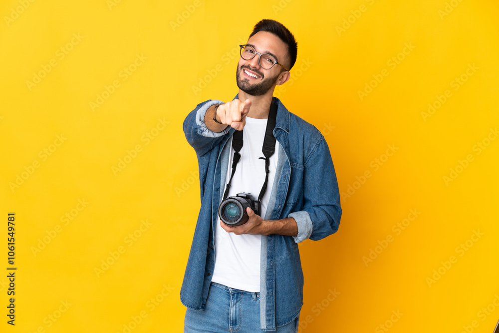 Young photographer girl isolated on yellow background pointing front with happy expression Young photographer girl isolated on yellow background pointing front with happy expression