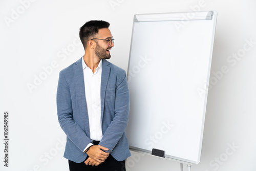 Young caucasian man isolated on white background giving a presentation on white board and looking side