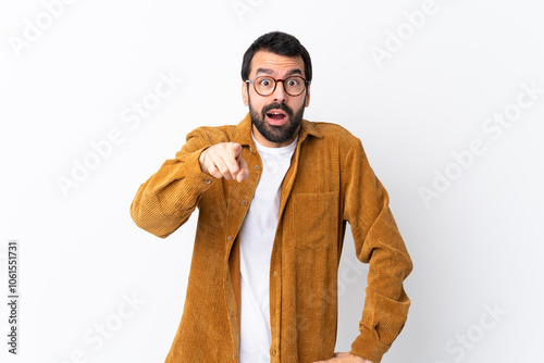 Caucasian handsome man with beard wearing a corduroy jacket over isolated white background surprised and pointing front