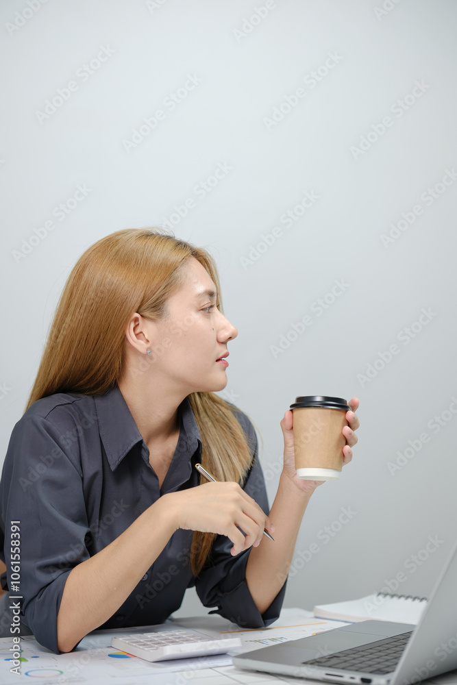 A woman is sitting at a desk with a laptop and a cup of coffee