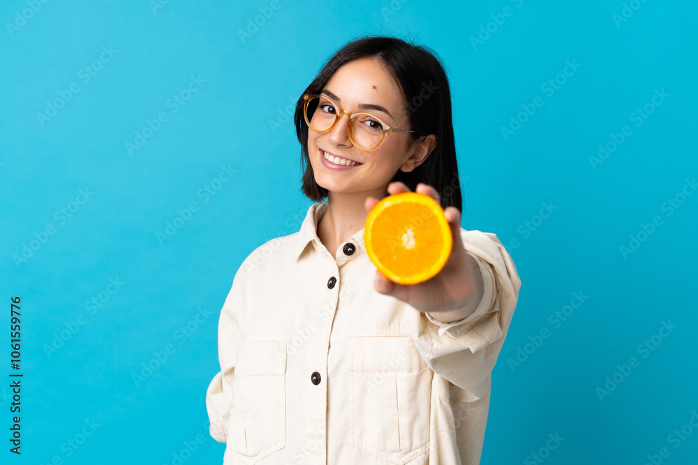 Young caucasian woman isolated on blue background holding an orange