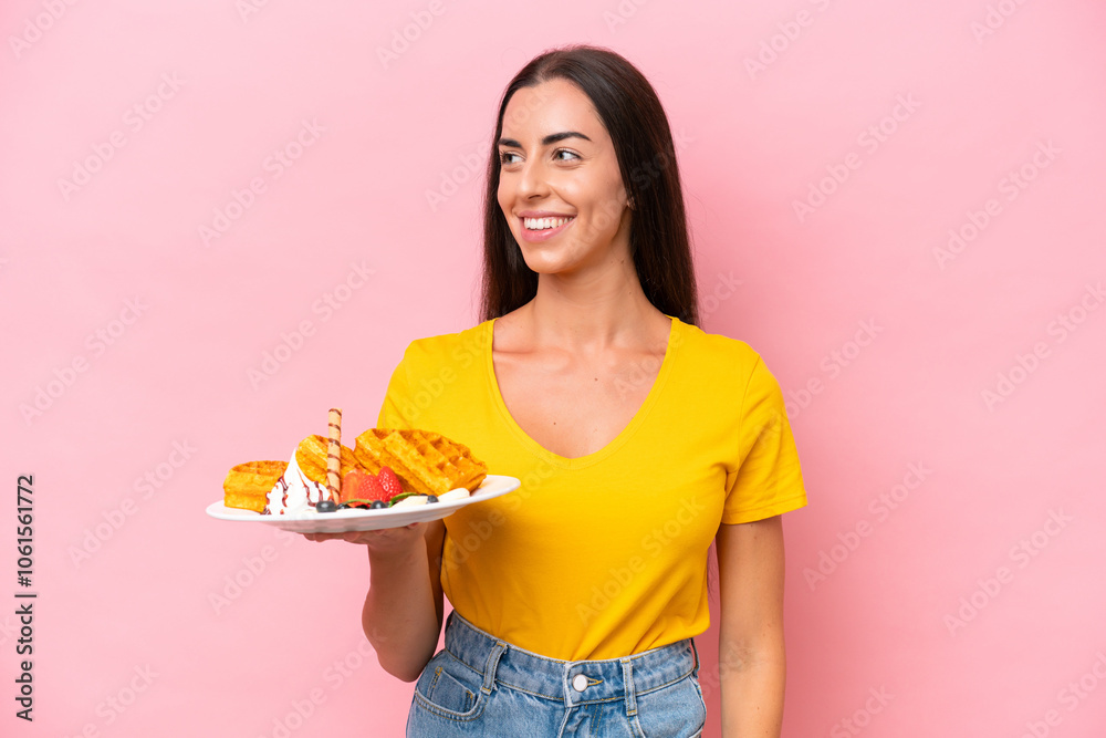 Young caucasian woman holding waffles isolated on pink background looking side Young caucasian woman holding waffles isolated on pink background looking side