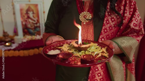 Cropped shot of anonymous woman in sari holding tray with burning diya during Diwali celebration indoors photo