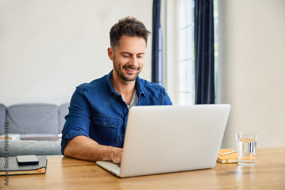 Happy man working on laptop at home sitting at table in living room Happy man working on laptop at home sitting at table in living room
